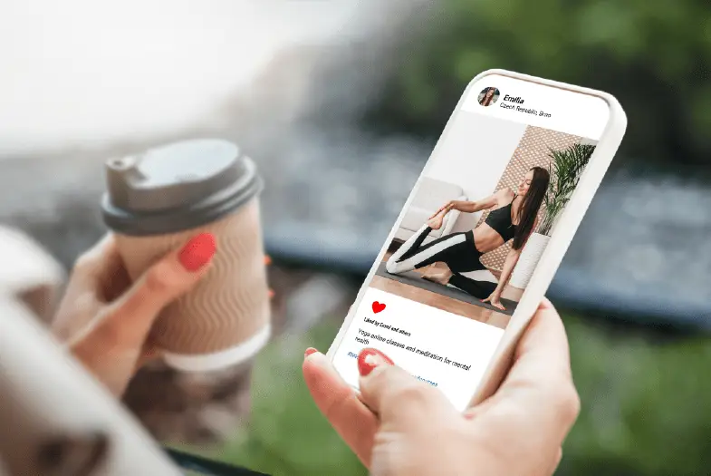 Woman holding a phone showing an image of a female influencer promoting fitness and wellness through her Instagram account