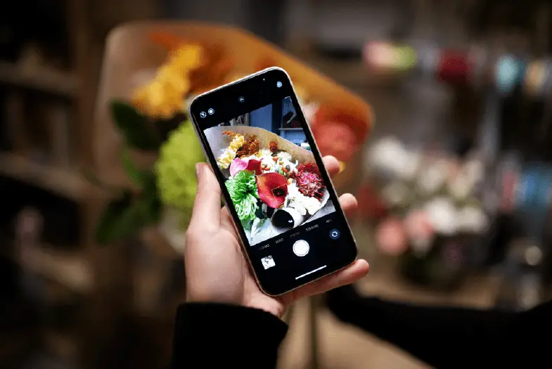 Person holding smartphone with flower bouquet in background