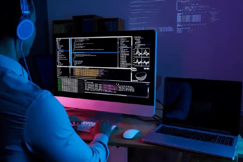 A man wearing headphones sits focused at a computer, engaged in web development activities.