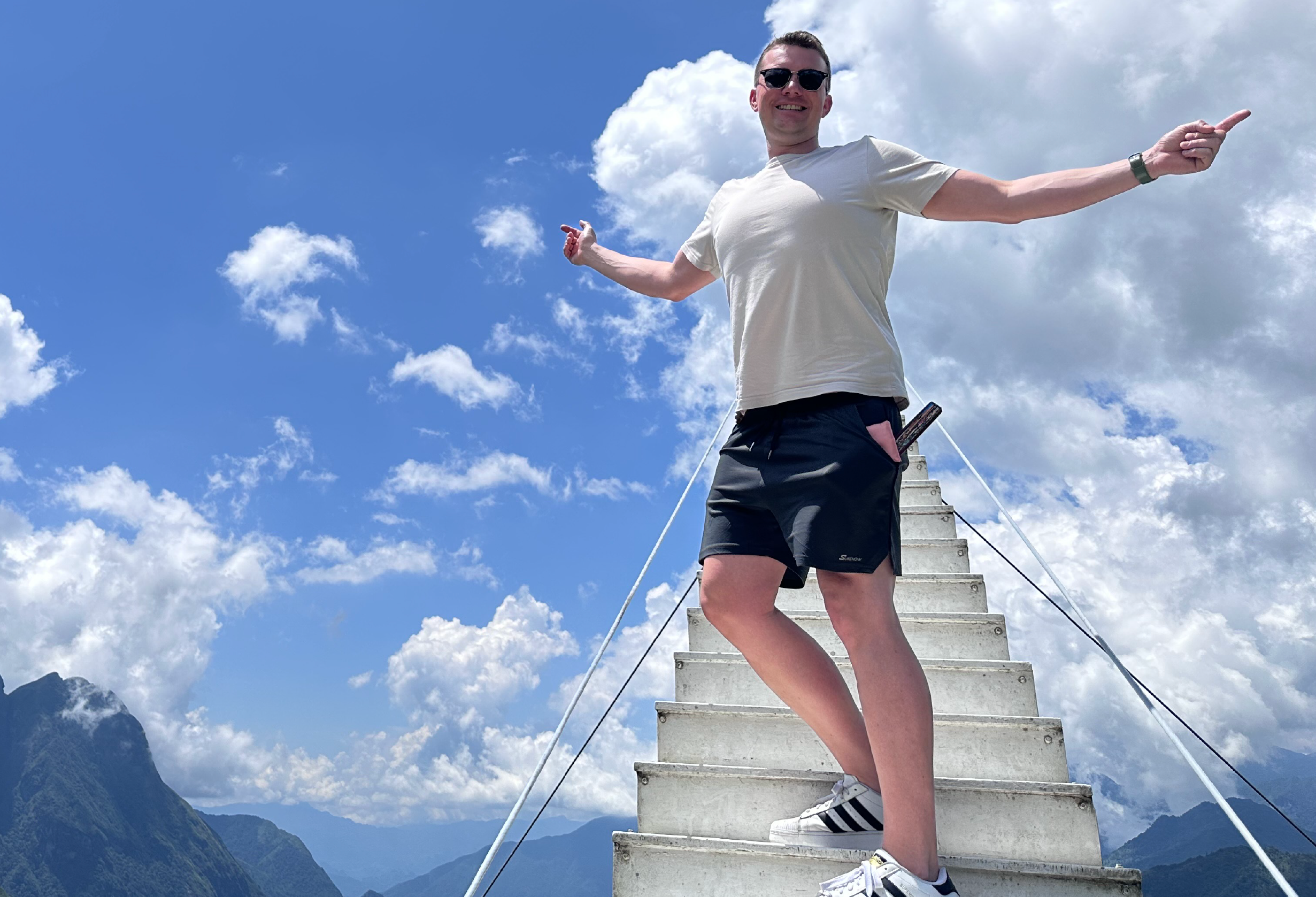 A man stands on a staircase, arms outstretched, embracing the moment with a confident and open posture.